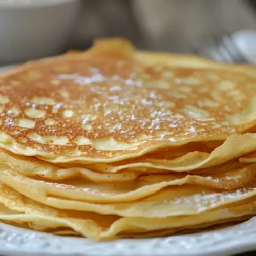 Une assiette de crêpes bretonnes dorées, légèrement saupoudrées de sucre, servie sur une table en bois rustique