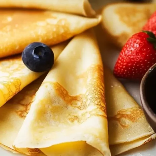 Assiette de crêpes sans gluten dorées , garnies de myrtilles, framboises et fraises, saupoudrées de sucre glace