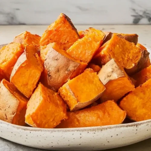 patate douce au four coupées en morceaux, servies dans une assiette en céramique avec une texture dorée et croustillante.